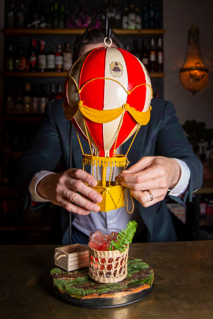 A decorative hot air balloon cake topper in red, yellow, and white, being handled by a person.