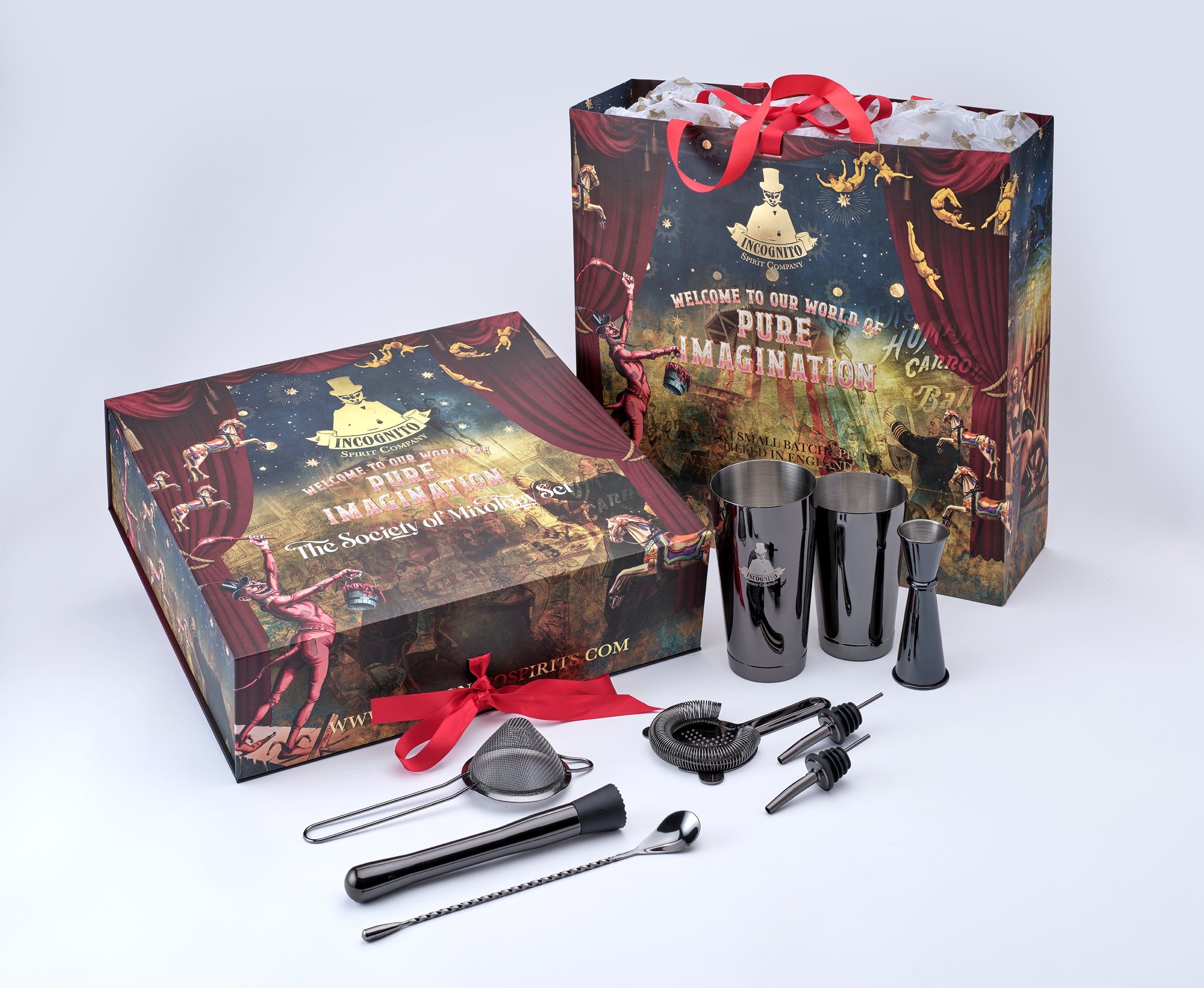 A bar gift set displayed on a light gray studio background, including a branded presentation box, a shopping bag, dark gray metal cocktail tumblers, a strainer, muddler, bar spoon, and bar tools, with red ribbon accents and theatrical-themed printed artwork.