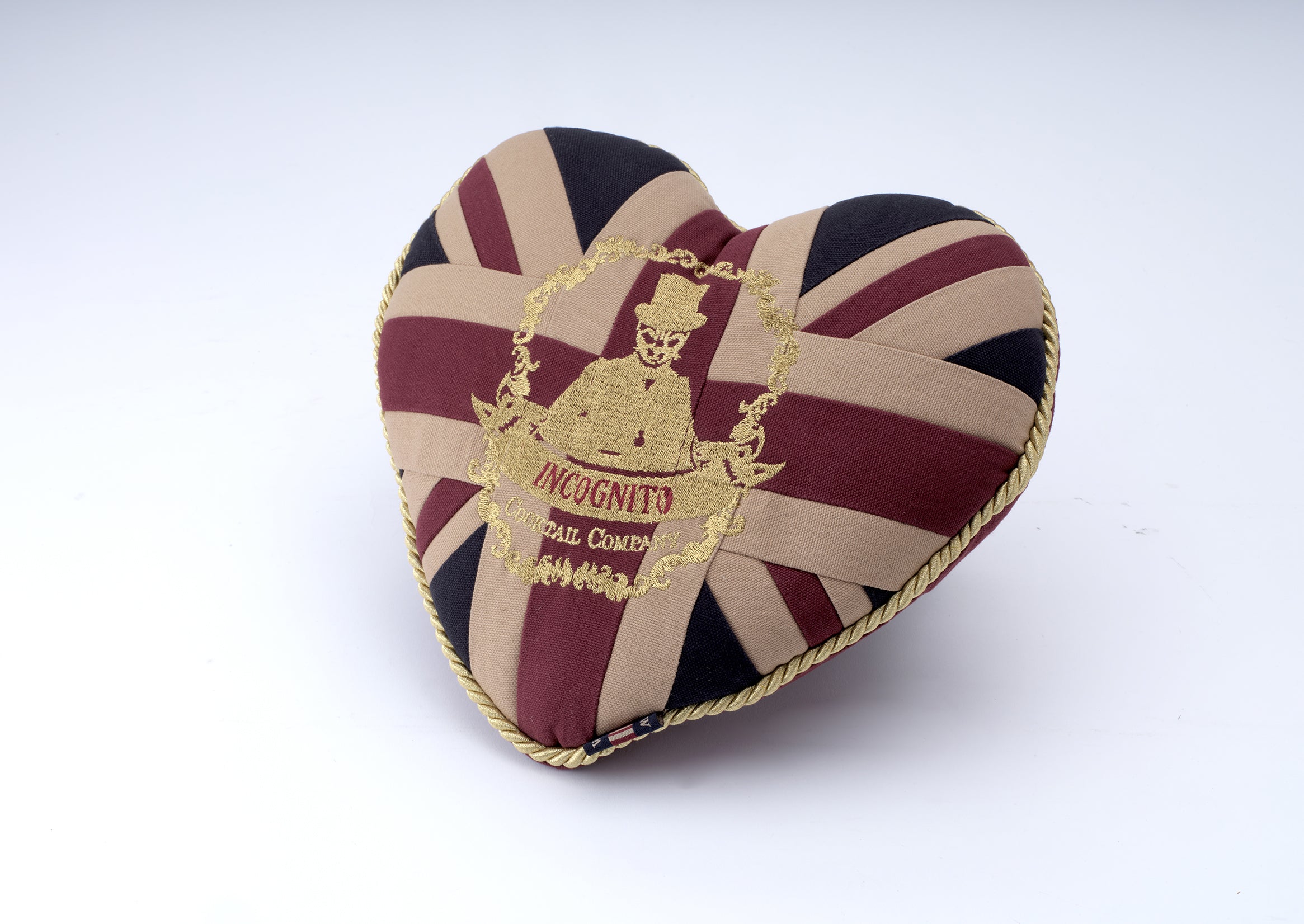 A heart-shaped fabric cushion featuring a Union Jack pattern in beige, burgundy, and black, with a gold embroidered crest in the center reading 'Insignity Ball Company' and a gold braided trim around the edge, shown on a white background.