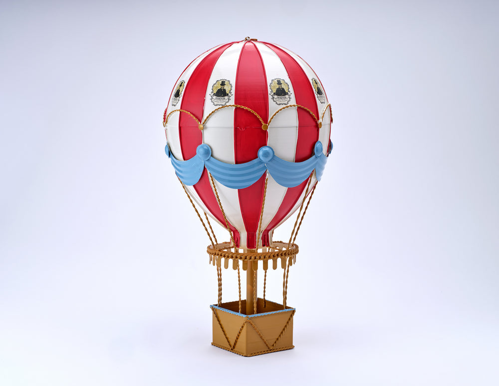 Incognito Hot Air Balloon ornament with red and white striped balloon, blue draping and gold detailing, presented with an illustrated Incognito gift box.