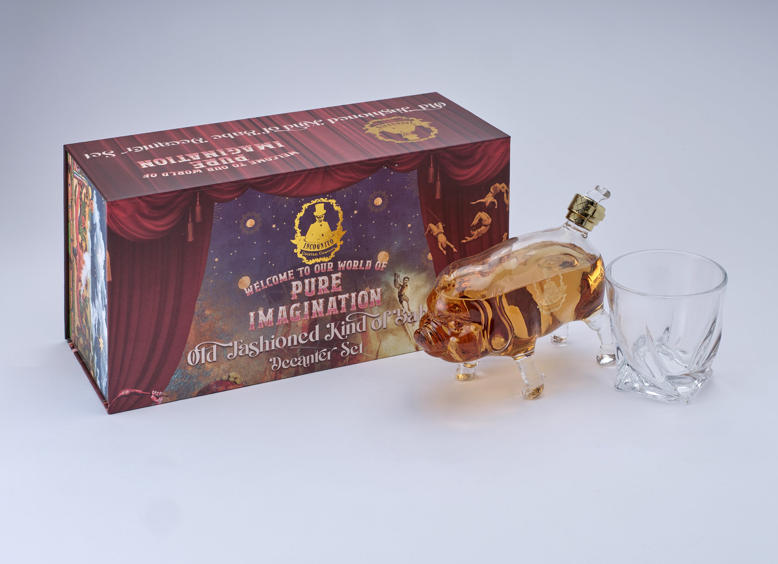 A novelty 'Pude Imagination' whiskey bottle shaped like a pig, filled with amber liquid and topped with a gold cap, shown next to a clear glass and its illustrated retail box on a light gray background.