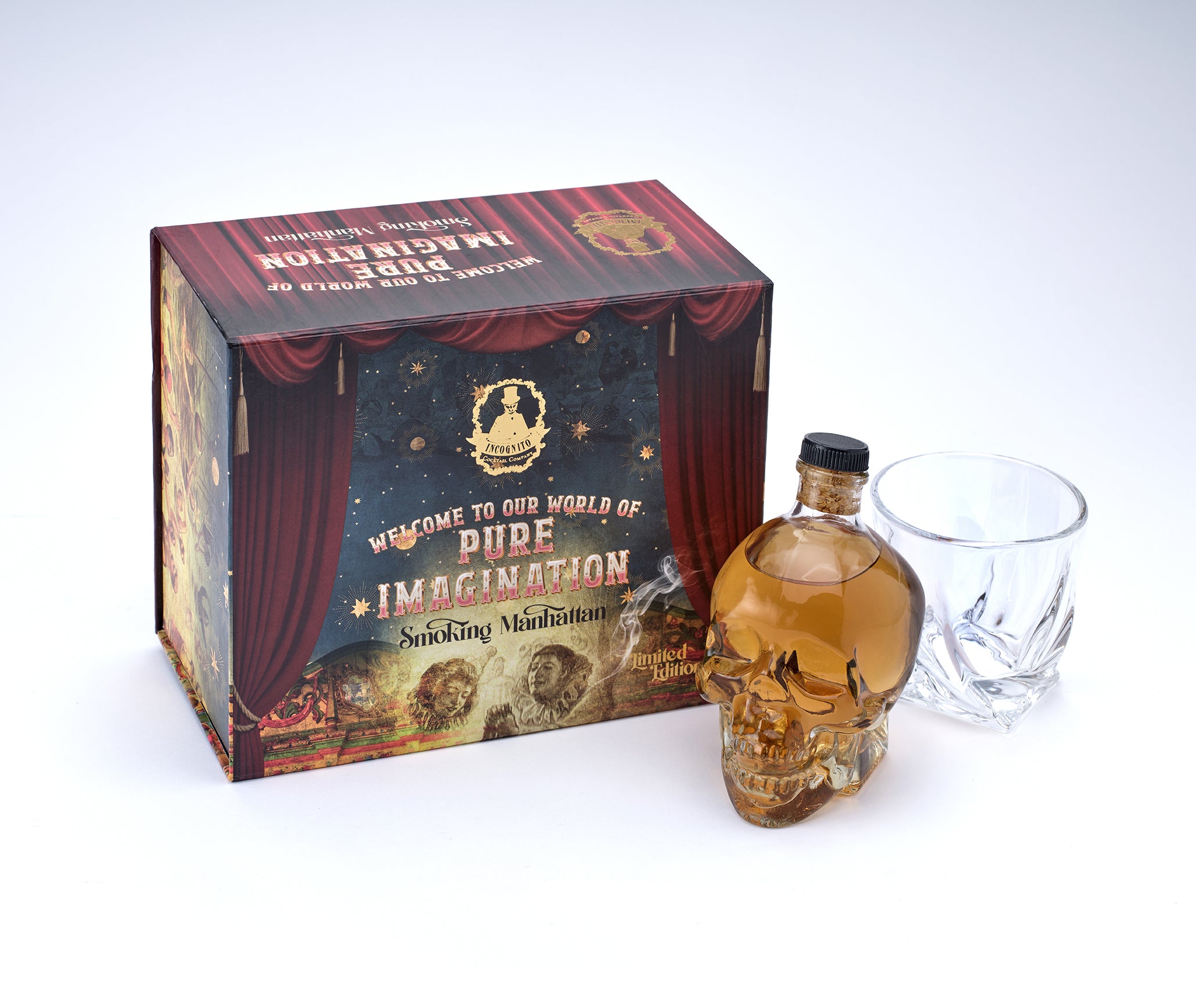 A skull-shaped bottle filled with amber liquid and a clear cut-glass tumbler, displayed beside a decorative branded box reading 'Pure Imagination Smoking Mixture' on a white studio background.