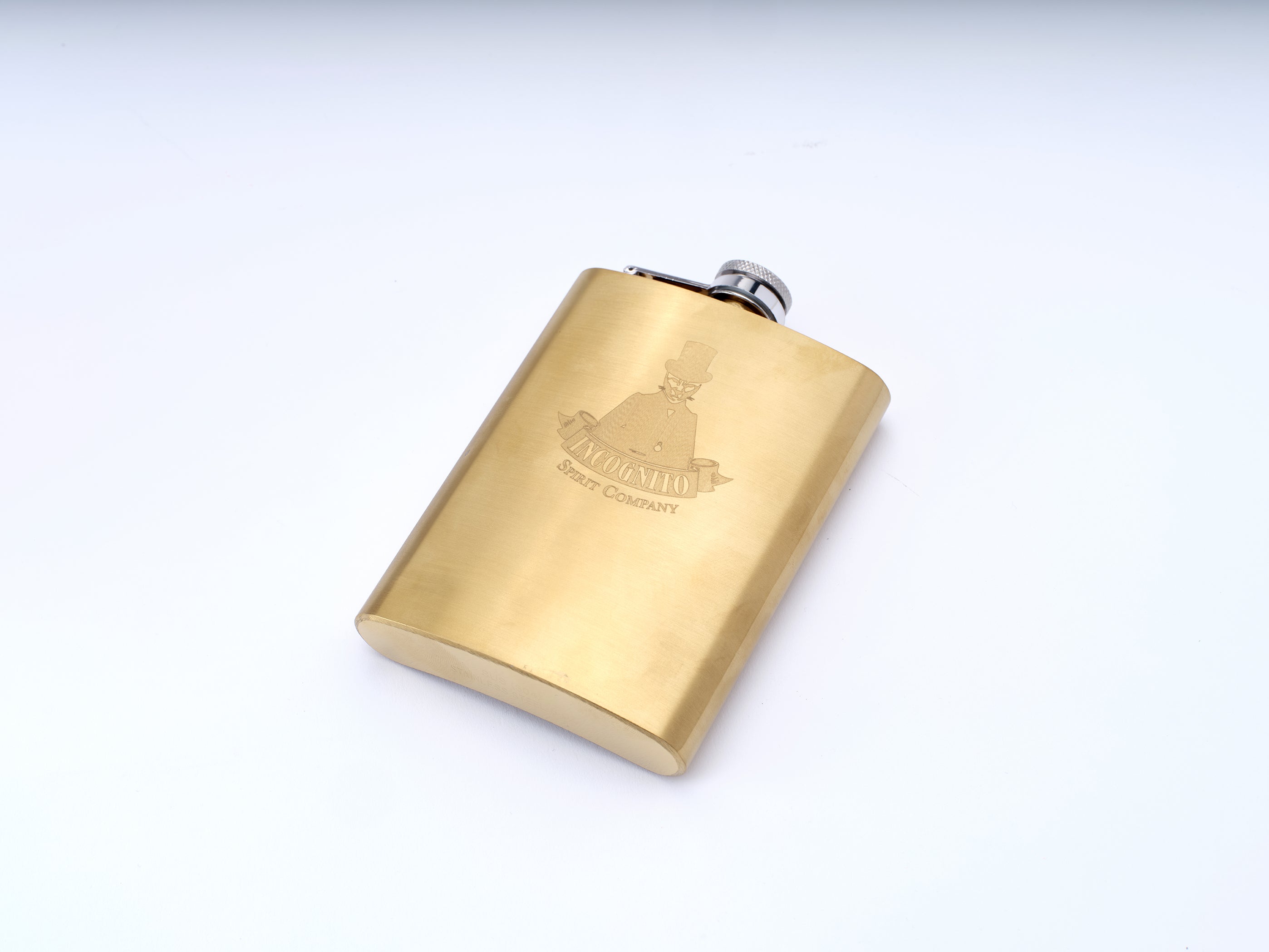 A square-shaped brass flask with a brushed gold finish, featuring an engraved Incognito spirit Company logo
