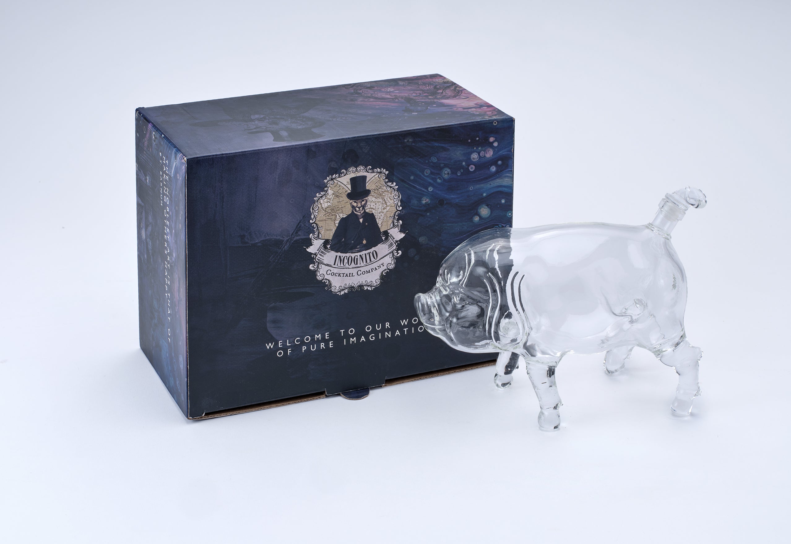 A clear glass pig figurine standing next to its dark blue illustrated retail box on a white background.