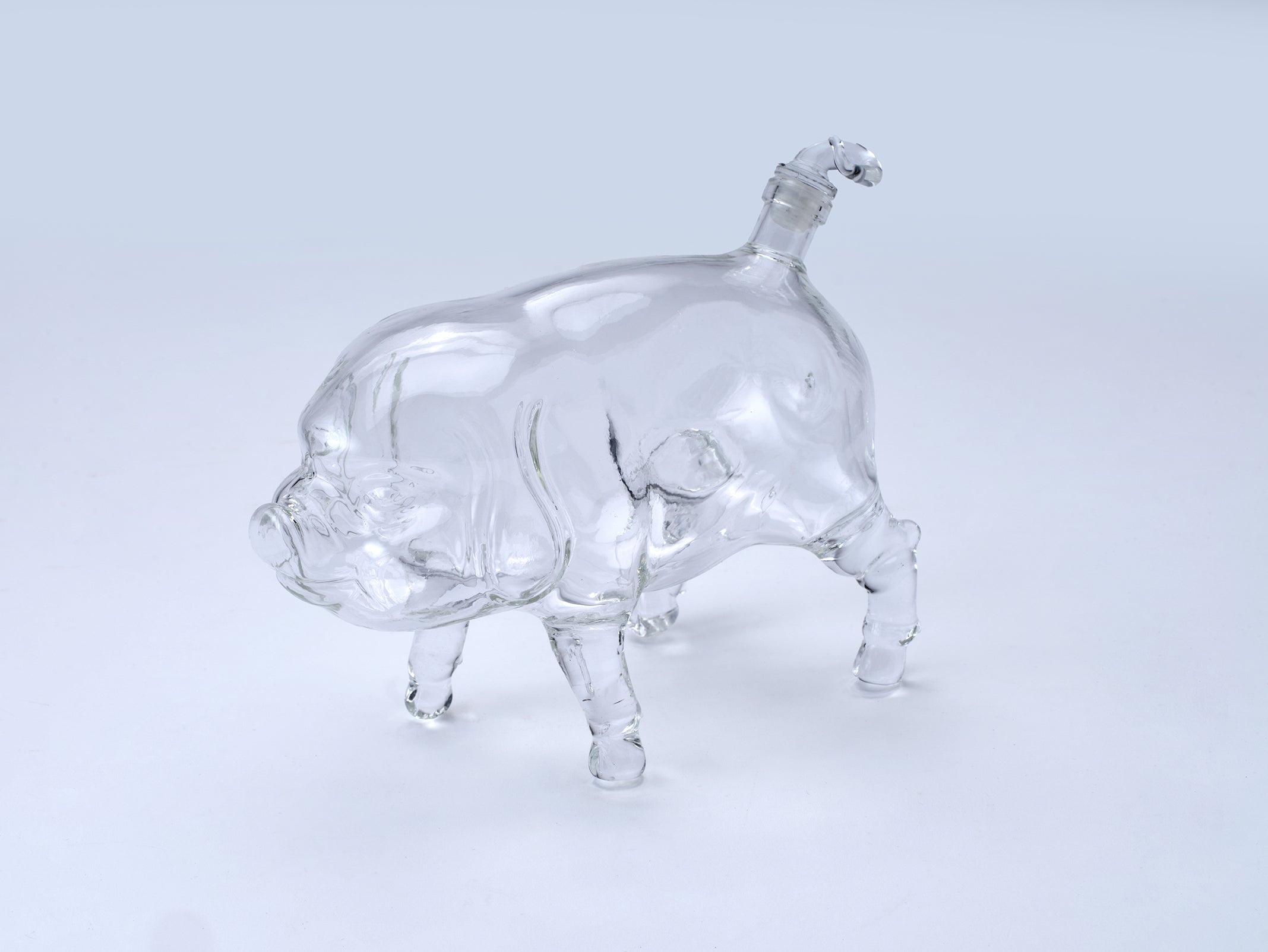 A clear glass pig figurine or bottle-shaped decorative object with a small neck opening at the top, photographed on a plain light gray studio background.