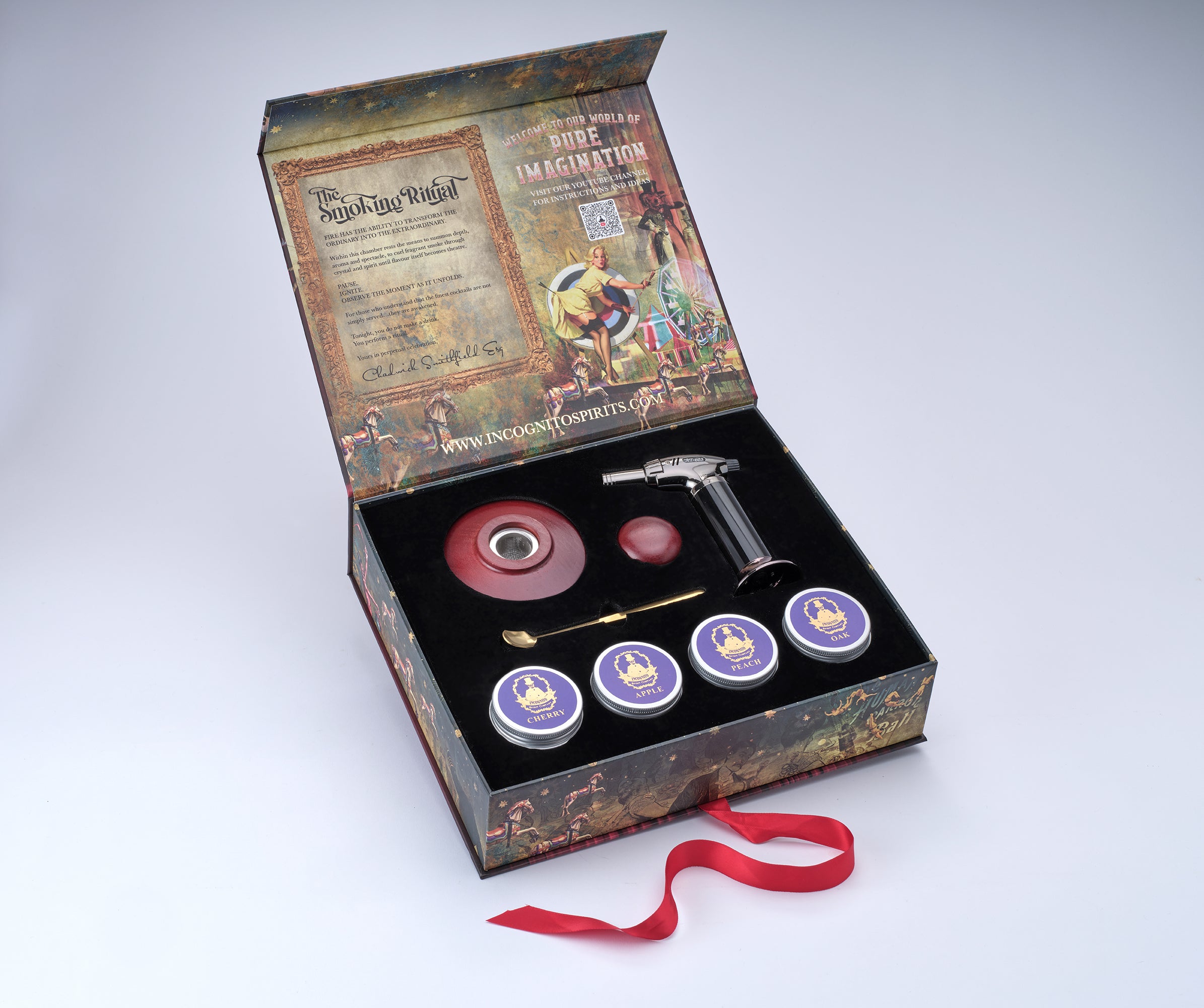 A Magic: The Gathering themed gift set displayed in an open decorative box on a light gray background. The set includes a black-handled torch lighter, a red circular component, a small red round piece, a gold-colored tool, three small round tins with purple lids, and a red ribbon in front of the box.